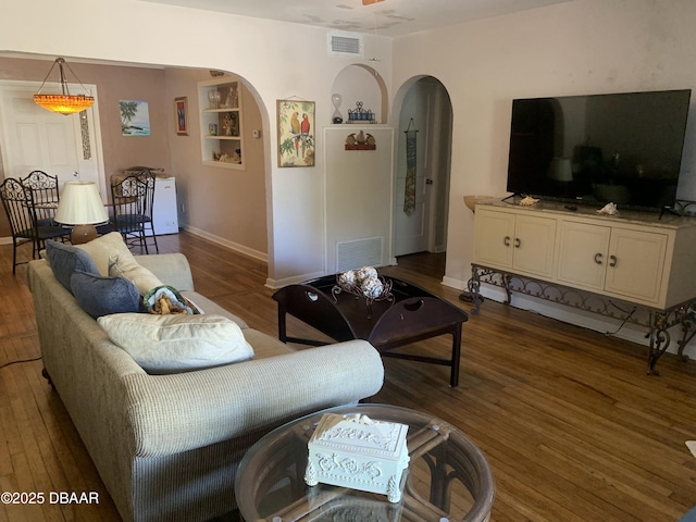 living area featuring arched walkways, visible vents, and wood finished floors