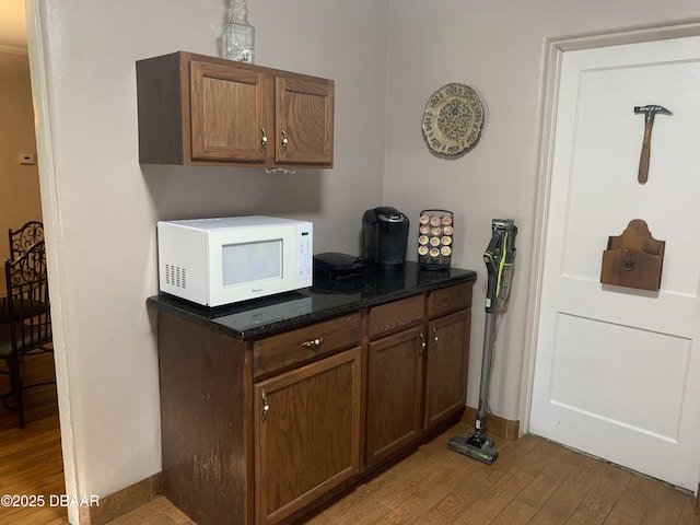 kitchen featuring white microwave, dark stone counters, and light wood finished floors