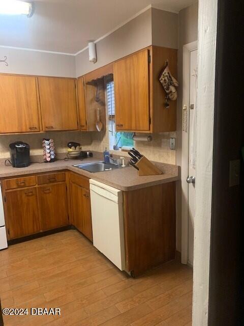 kitchen featuring brown cabinetry, white dishwasher, a sink, and light wood-style flooring