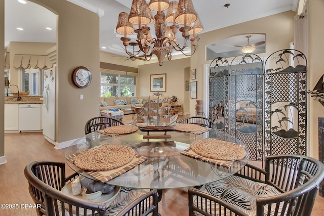 dining space with sink, ceiling fan with notable chandelier, and light wood-type flooring