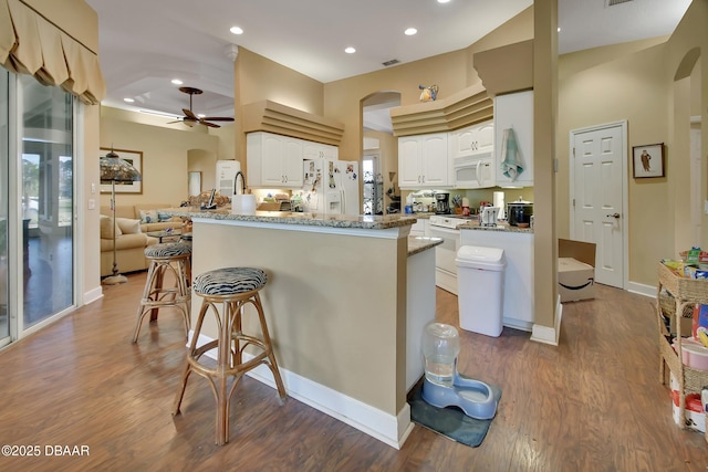 kitchen with a breakfast bar, stone countertops, white cabinetry, kitchen peninsula, and white appliances