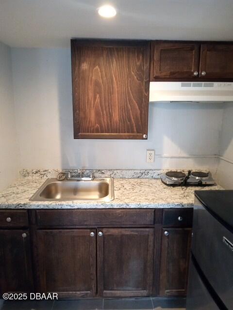 kitchen featuring light stone counters, sink, and dark brown cabinets