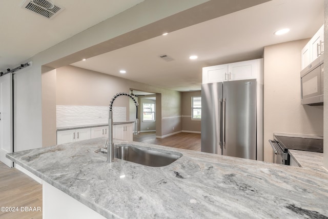 kitchen with light stone counters, a barn door, sink, white cabinetry, and appliances with stainless steel finishes