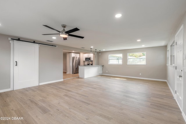 unfurnished living room with light hardwood / wood-style floors, a barn door, and ceiling fan