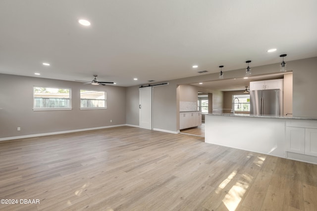 unfurnished living room featuring a barn door, ceiling fan, and light wood-type flooring