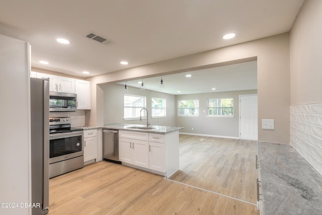 kitchen with appliances with stainless steel finishes, sink, light hardwood / wood-style floors, white cabinets, and kitchen peninsula