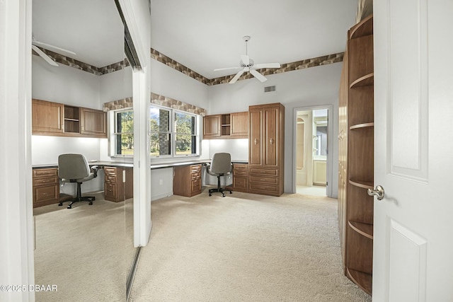 carpeted office space with built in desk and ceiling fan