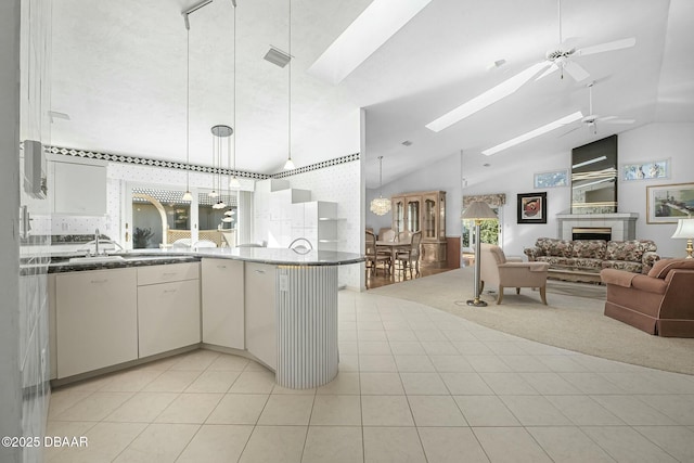 kitchen featuring ceiling fan, light colored carpet, vaulted ceiling with skylight, hanging light fixtures, and white cabinets