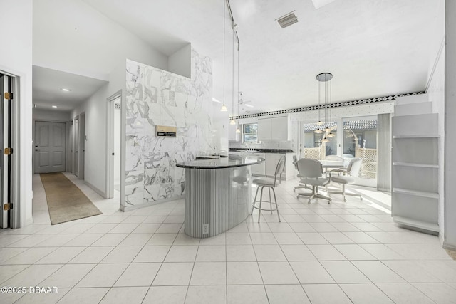 kitchen featuring a center island, pendant lighting, a kitchen bar, light tile patterned flooring, and white cabinets