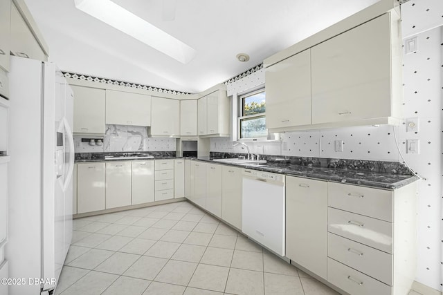 kitchen with white appliances, dark stone counters, sink, light tile patterned floors, and lofted ceiling with skylight