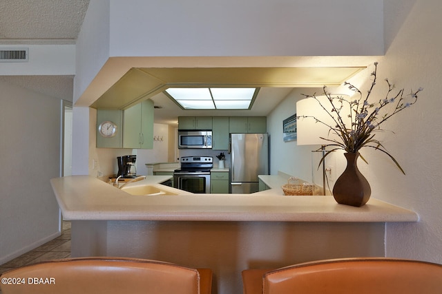 kitchen with green cabinetry, kitchen peninsula, sink, light tile patterned flooring, and appliances with stainless steel finishes