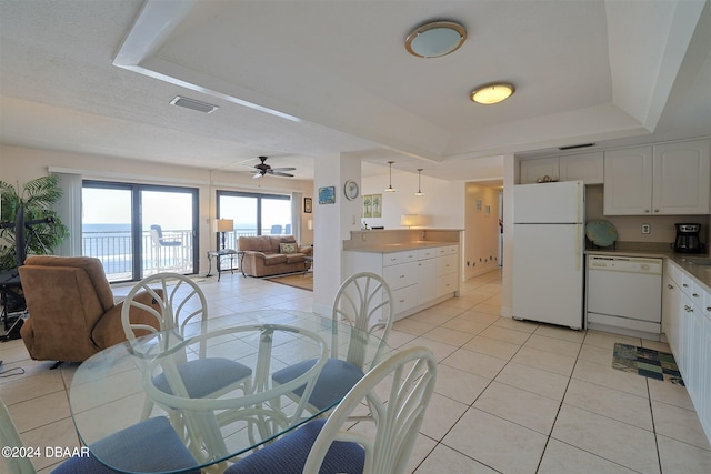 dining area featuring a water view, light tile patterned floors, ceiling fan, and a raised ceiling