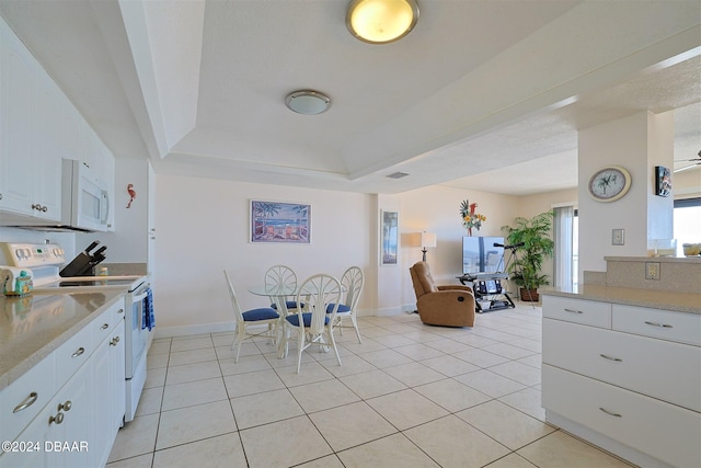 kitchen featuring white cabinetry, light tile patterned floors, white appliances, and a tray ceiling