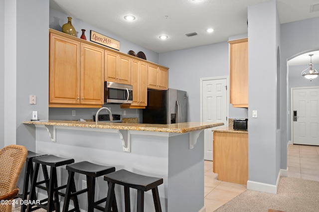 kitchen featuring kitchen peninsula, light stone counters, a breakfast bar, and appliances with stainless steel finishes