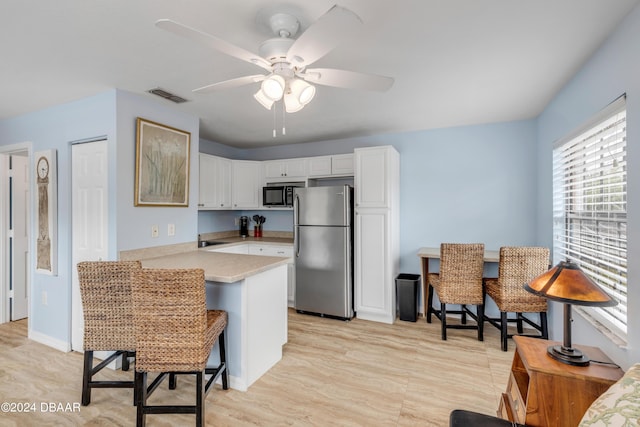 kitchen with white cabinetry, a kitchen breakfast bar, stainless steel fridge, kitchen peninsula, and ceiling fan