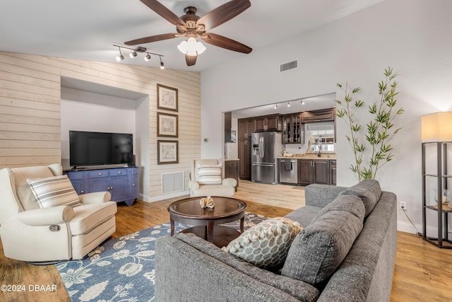 living room with rail lighting, wooden walls, ceiling fan, and light hardwood / wood-style floors