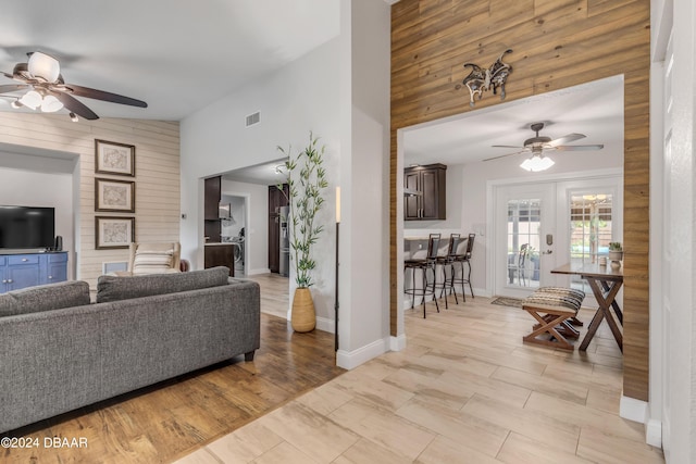 living room featuring light hardwood / wood-style floors, wooden walls, high vaulted ceiling, and french doors