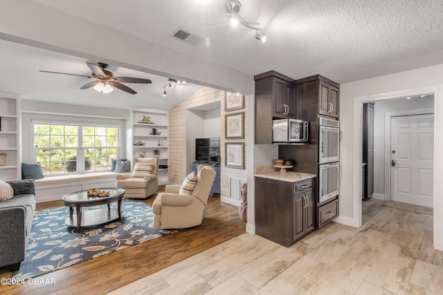 living room with built in features, ceiling fan, a textured ceiling, vaulted ceiling, and light wood-type flooring