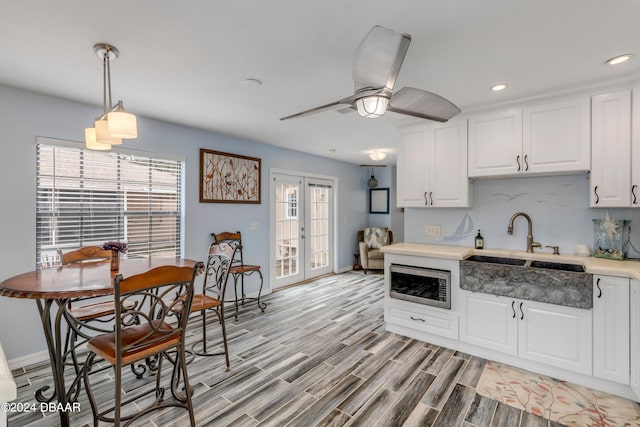 kitchen with stainless steel microwave, decorative light fixtures, white cabinetry, sink, and french doors