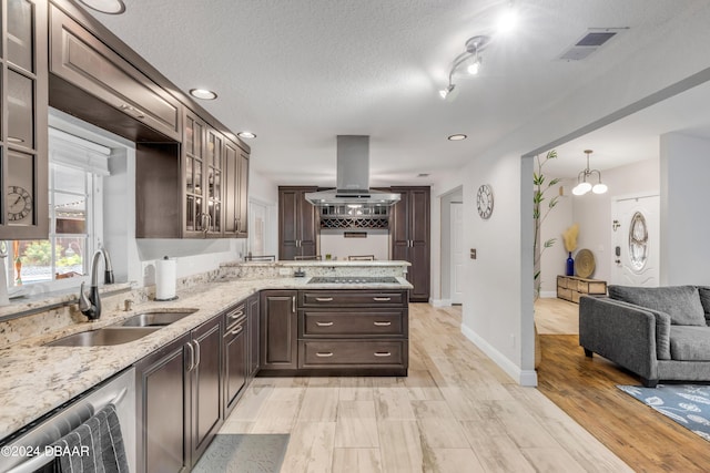 kitchen with light stone countertops, island exhaust hood, dark brown cabinets, and sink