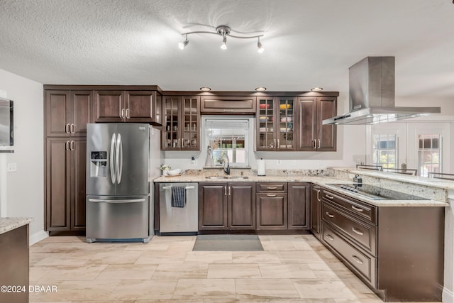 kitchen featuring dark brown cabinetry, sink, light stone counters, island range hood, and appliances with stainless steel finishes