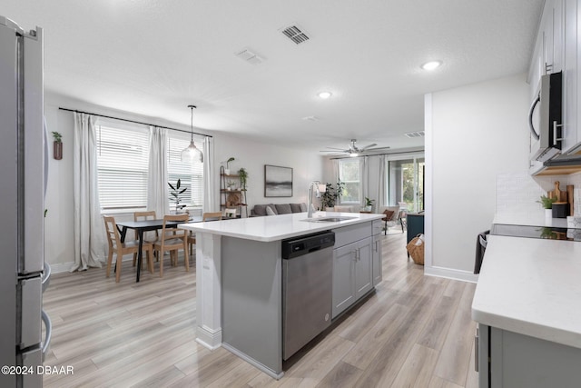 kitchen with appliances with stainless steel finishes, ceiling fan, decorative light fixtures, a center island with sink, and gray cabinets