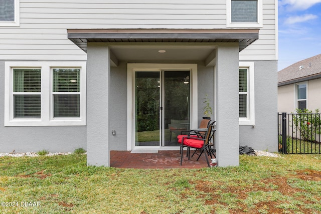 view of exterior entry featuring a patio and a lawn