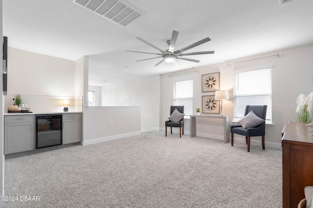 living area featuring light carpet, ceiling fan, beverage cooler, and a textured ceiling