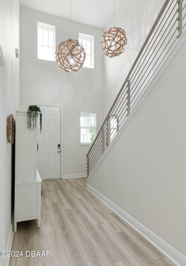 entryway with a high ceiling, light wood-type flooring, and an inviting chandelier