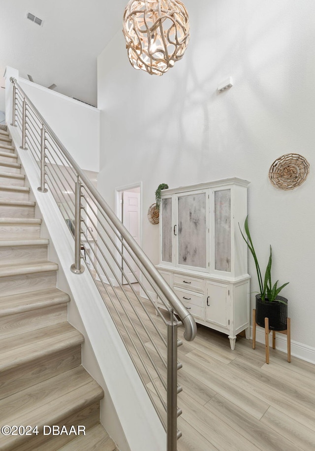 stairway featuring a notable chandelier, wood-type flooring, and a high ceiling