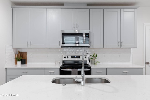 kitchen with backsplash, light stone counters, sink, and appliances with stainless steel finishes