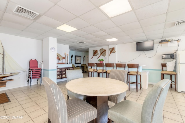 dining area with a drop ceiling and light tile patterned flooring