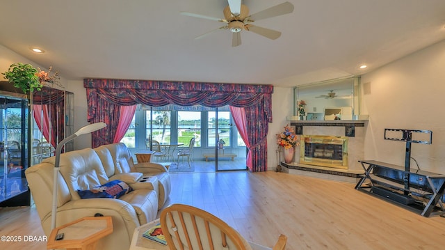 living room featuring wood-type flooring, a stone fireplace, and ceiling fan