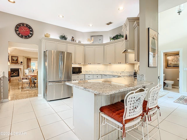 kitchen with kitchen peninsula, light stone counters, a kitchen breakfast bar, light tile patterned floors, and stainless steel fridge