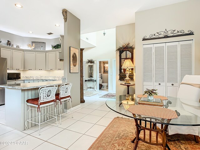 kitchen with light stone counters, a breakfast bar area, gray cabinetry, light tile patterned flooring, and stainless steel fridge