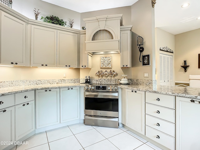 kitchen featuring stainless steel range with electric stovetop, light tile patterned flooring, premium range hood, and light stone countertops