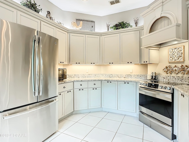 kitchen featuring cream cabinets, light stone counters, light tile patterned flooring, appliances with stainless steel finishes, and custom range hood