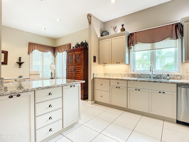 kitchen featuring light stone counters, light tile patterned floors, sink, dishwasher, and cream cabinetry