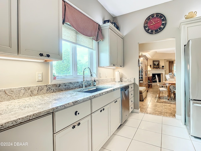 kitchen with stainless steel appliances, light tile patterned flooring, white cabinetry, sink, and light stone counters