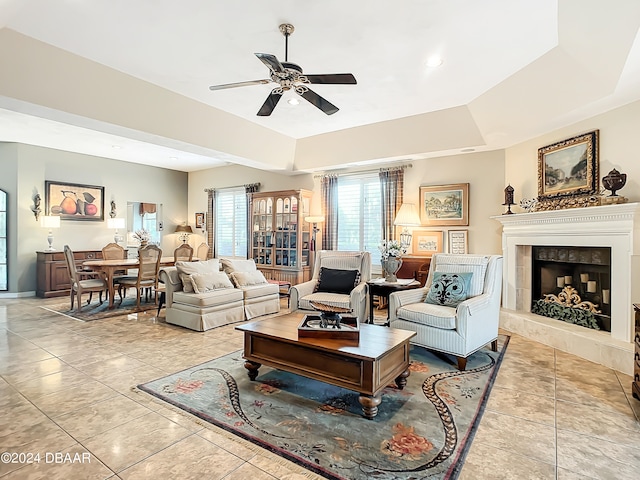 tiled living room featuring a fireplace, ceiling fan, and a raised ceiling