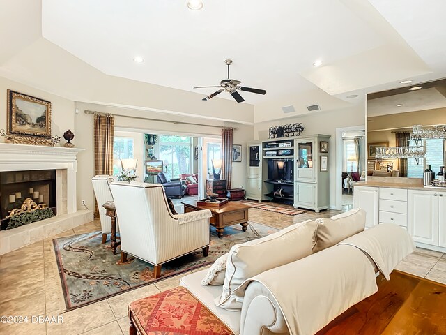 living room with a tiled fireplace, bar area, ceiling fan, light tile patterned flooring, and a tray ceiling