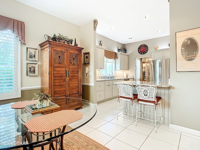 kitchen featuring light tile patterned flooring, sink, stainless steel refrigerator, and a breakfast bar area