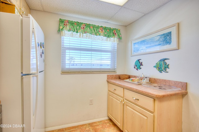 kitchen with light brown cabinetry, white refrigerator, light tile patterned floors, and a paneled ceiling