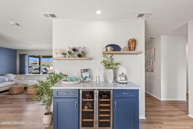 bar featuring blue cabinets, beverage cooler, light hardwood / wood-style flooring, and a textured ceiling