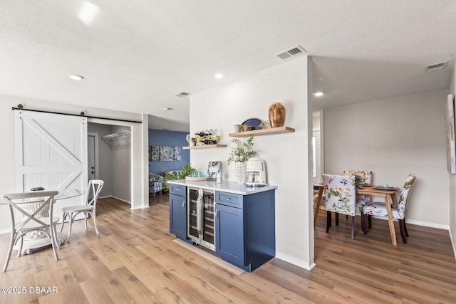 kitchen with a barn door, blue cabinetry, wine cooler, and light hardwood / wood-style floors