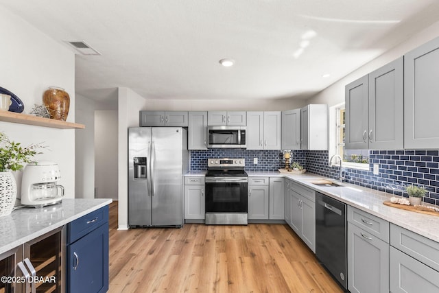 kitchen with sink, light wood-type flooring, stainless steel appliances, light stone countertops, and decorative backsplash