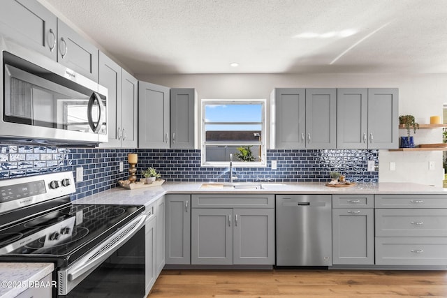 kitchen with stainless steel appliances, light wood-type flooring, gray cabinetry, and light stone counters