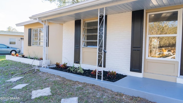 entrance to property featuring a porch and brick siding