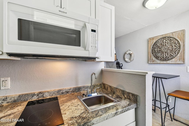 kitchen featuring stovetop, white cabinetry, sink, and dark stone counters