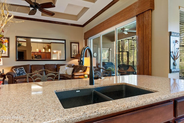 kitchen featuring light stone counters, ceiling fan, ornamental molding, and sink